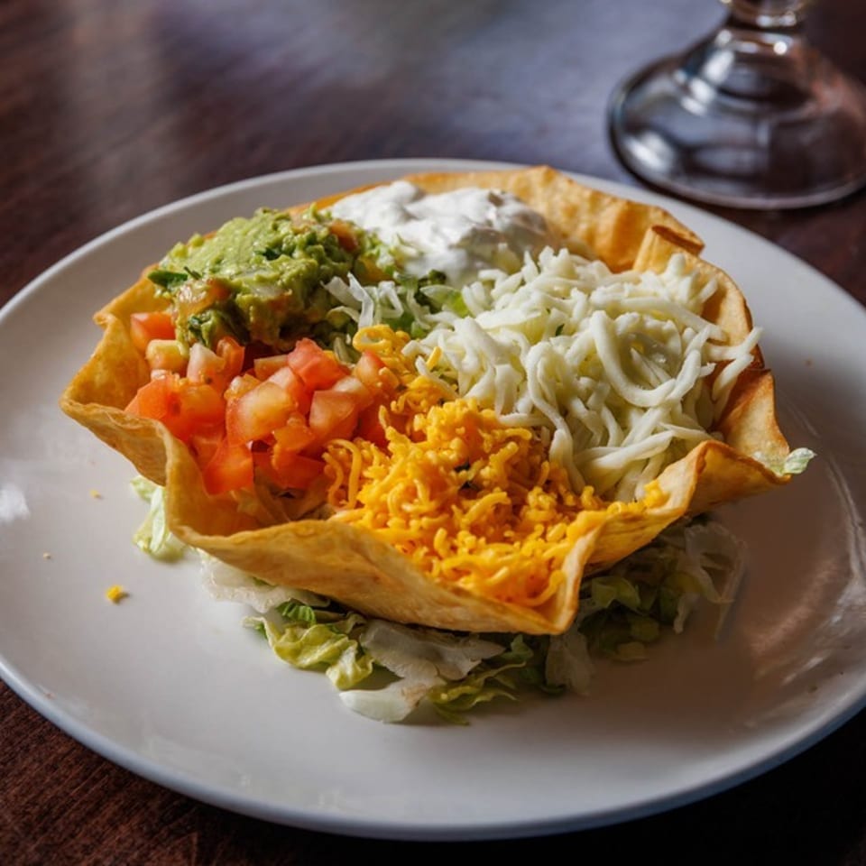 Taco salad in a crispy tortilla bowl with guacamole, diced tomatoes, and shredded cheese.