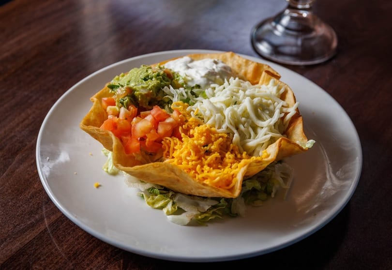 Taco salad in a crispy tortilla bowl with guacamole, diced tomatoes, and shredded cheese.